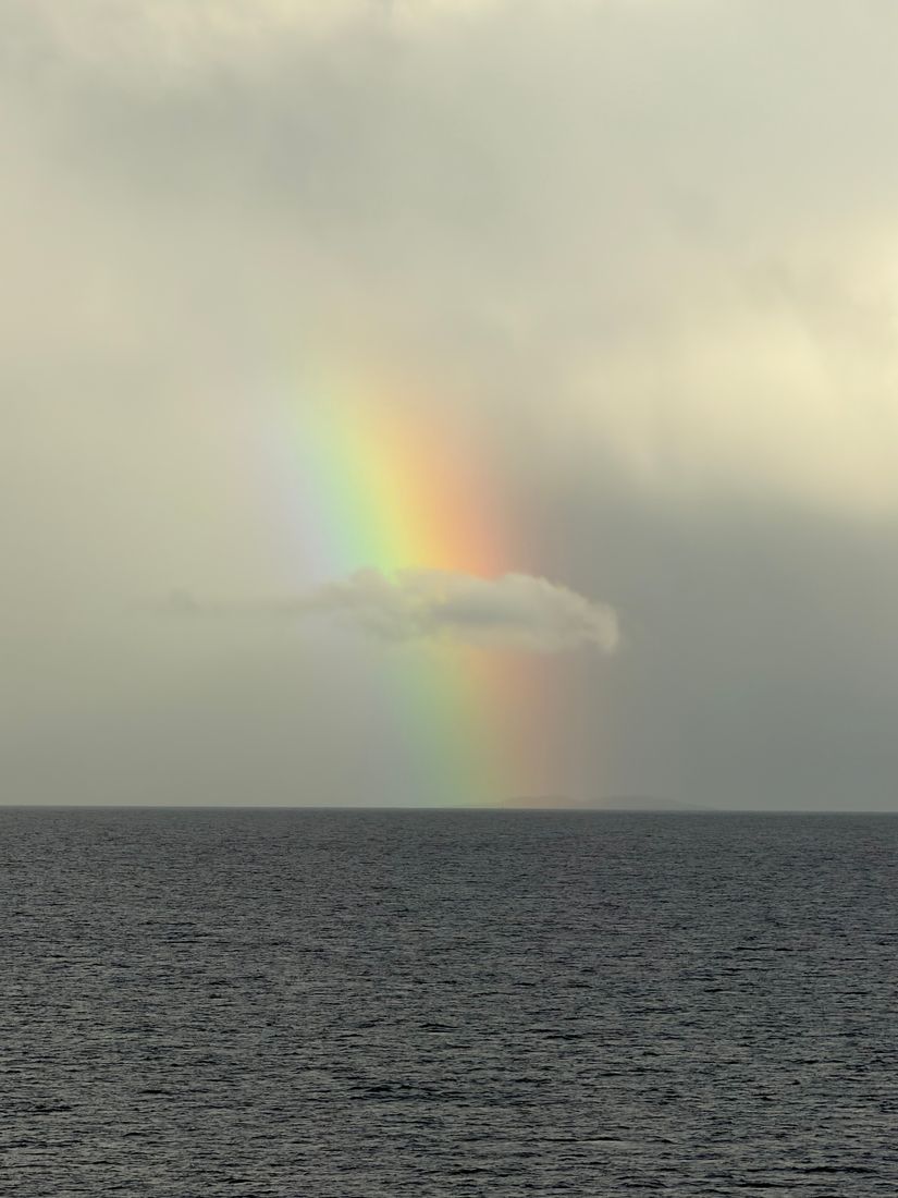 Rainbow dropping into a dark sea under heavy rain clouds