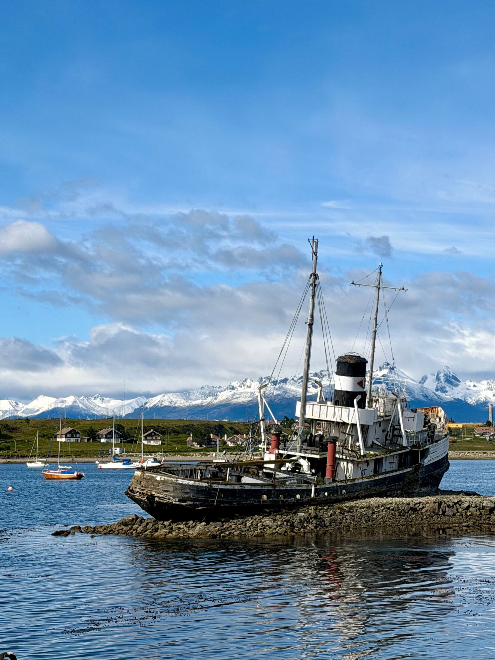 Old steamship aground on rocks in a harbour, snowy mountains behind