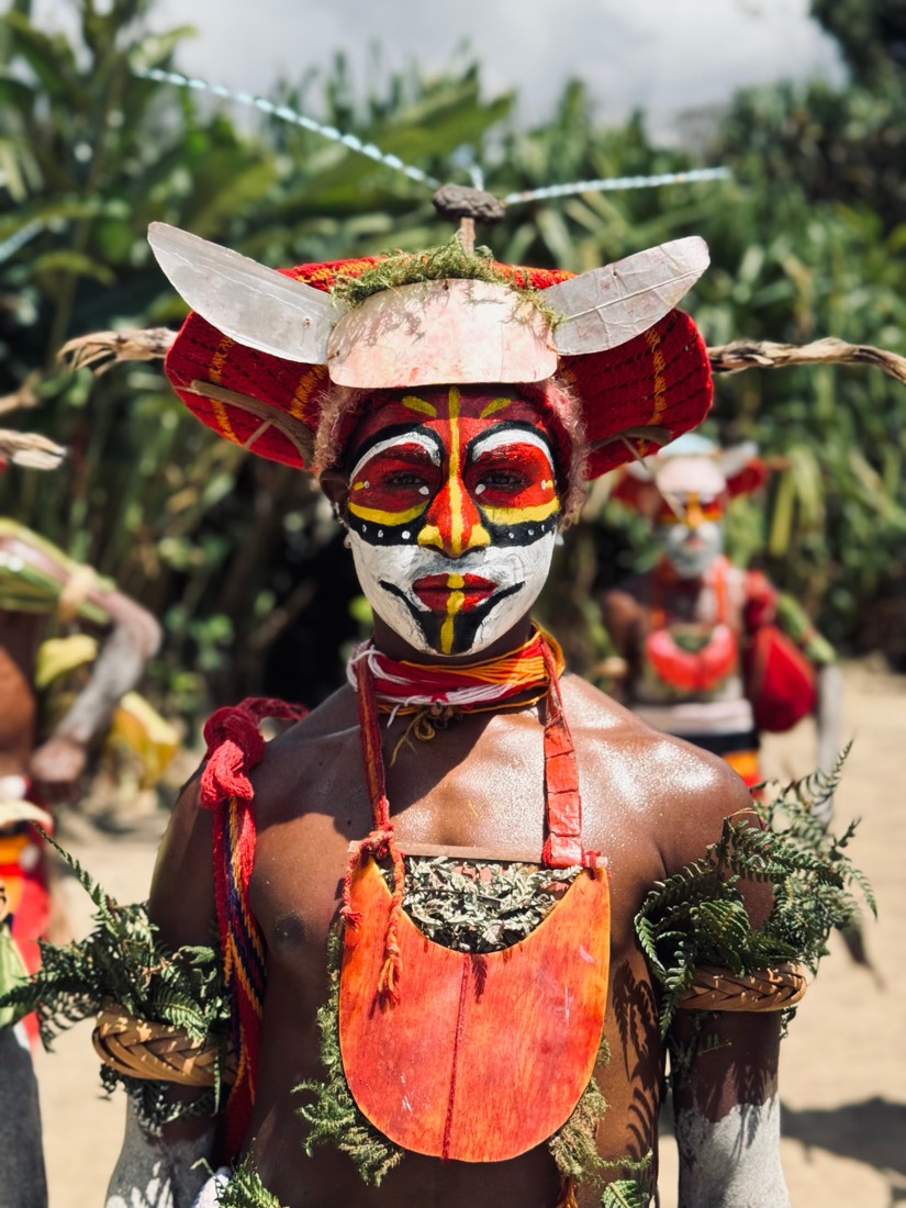 A Highlands dancer in a red and white painted face and a horned headdress of bark and feathers at a sing-sing in Papua New Guinea