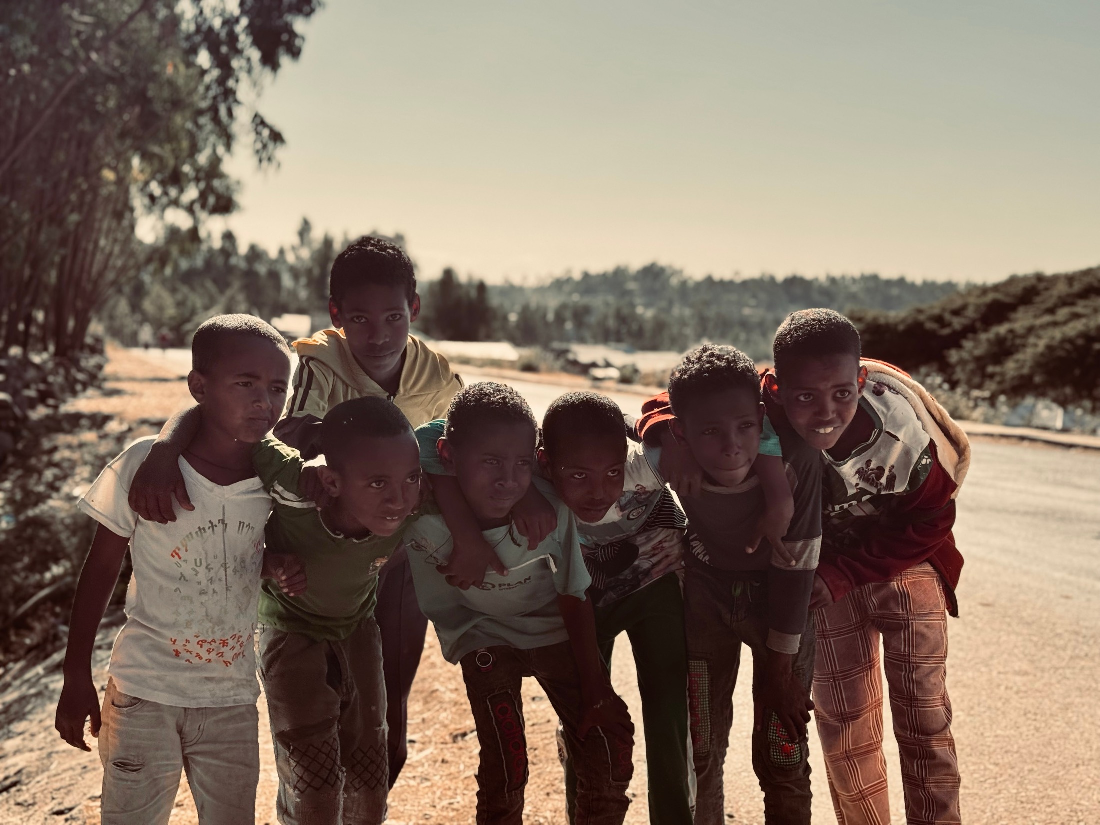 A crowd of boys leaning in together on a dusty highland road in northern Ethiopia, laughing at the camera